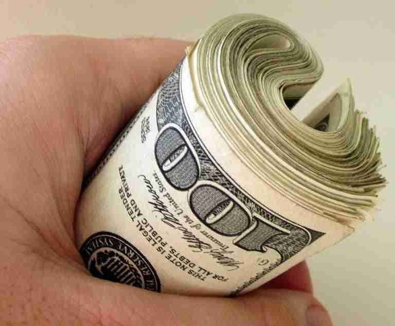 A hand holding a thick roll of US dollar bills, suggesting the best concept of wealth or savings.
