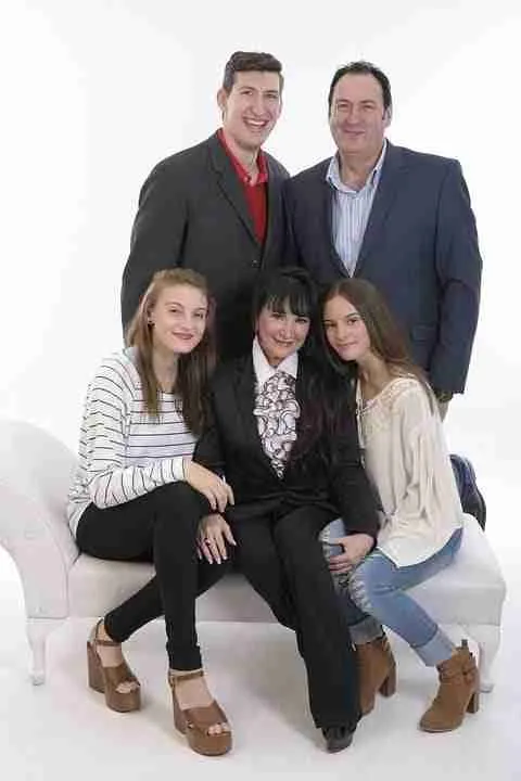 A happy family portrait featuring two parents standing behind a white sofa where their three smiling daughters, living with their parents after getting a loan, are seated.