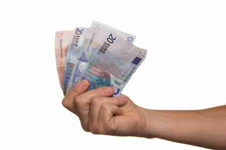 A hand holding a selection of euro banknotes indicating the need for a 500 loan against a white background.
