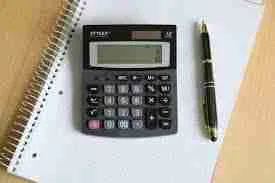A scientific calculator next to a pen on top of a spiral notebook, all necessary for someone planning to calculate their budget and need a 6000 loan.