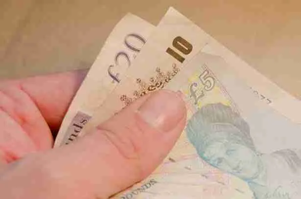 Hand holding British currency notes including a £5, £10, and £20 bill for 15000 guarantor loans.