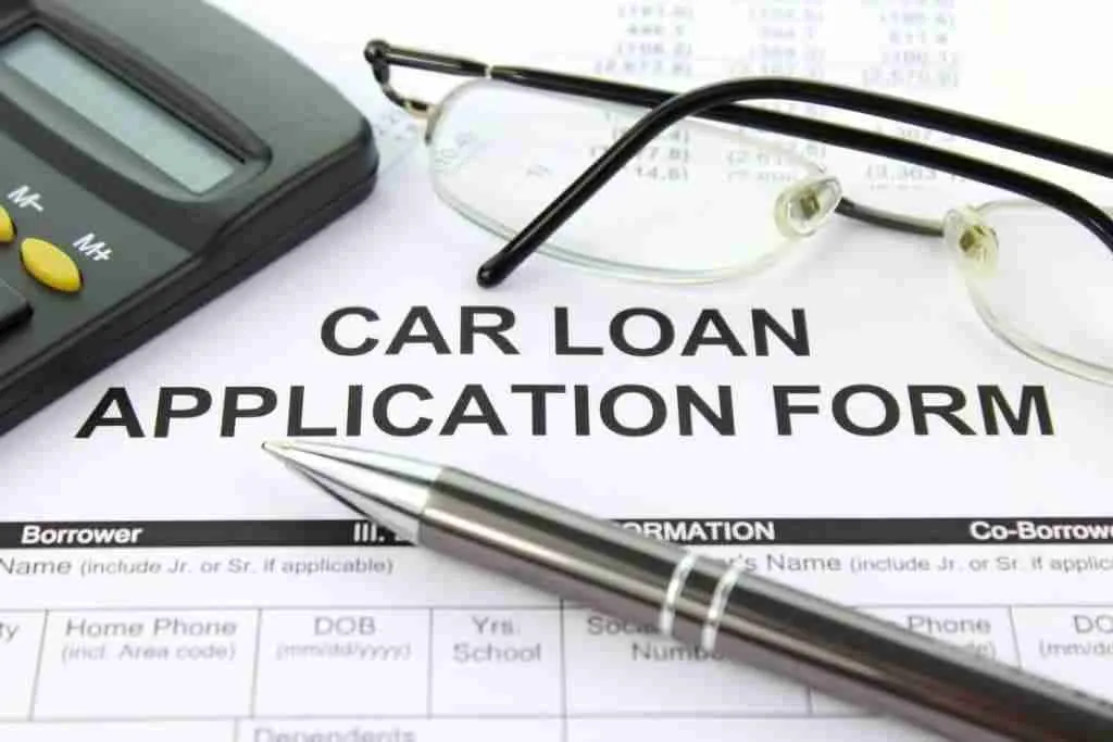 A pen, a pair of glasses, and a calculator resting on top of a car loan application form, symbolizing financial planning and loan application for vehicle purchase.