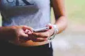 A person standing and using a smartphone, carefully reviewing mobile phone contracts for bad credit with a focus on their hands and the device.