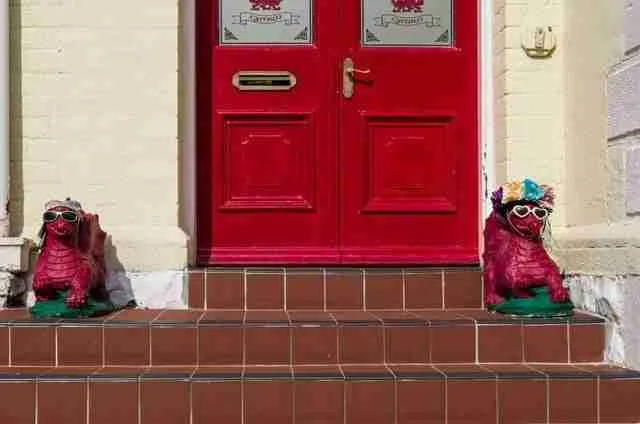 Two quirky, colorful statues of creatures wearing sunglasses flank a vibrant red double door, creating a whimsical and welcoming entrance to the same day doorstep loans office.