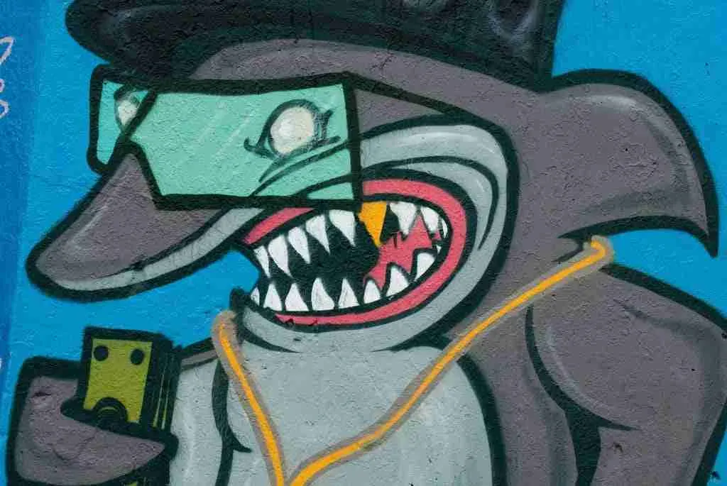 Graffiti art of a stylized, cartoon-like character with a toothy grin, wearing a hat and sunglasses, holding what appears to be a camera, surrounded by loan sharks.