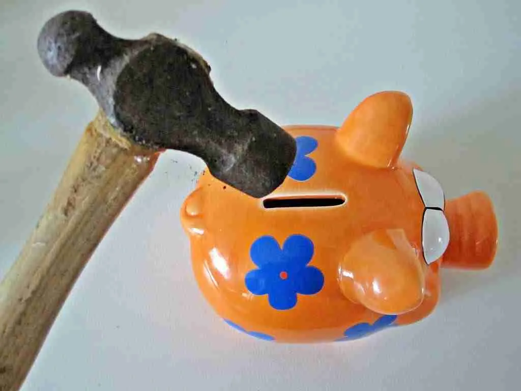 An orange ceramic piggy bank adorned with blue flowers, symbolizing the precarious nature of relying on payday loans direct lenders, is about to be struck by a hammer to access saved money.
