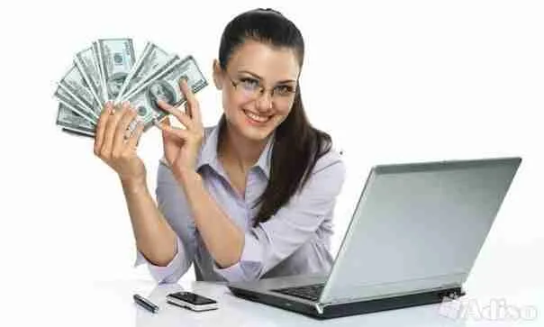 A smiling woman sitting at a desk with a laptop, showcasing a fan of cash in her hands received from a direct loan lender, possibly representing financial success or online business achievement.