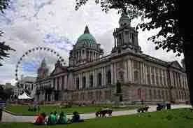 An imposing historic building with a large dome and classical architecture, flanked by green trees advertising payday loans in Northern Ireland, with a giant ferris wheel in the background under a cloudy sky.