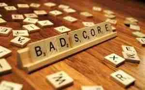Scrabble tiles on a wooden rack spelling out "bad credit" with more letter tiles scattered on the table, possibly after a tough round of wordplay.
