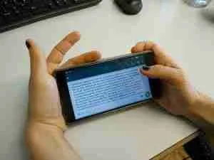 A person holding a smartphone with both hands, displaying a text conversation about how to get a contract phone with bad credit on the screen, over a desk with a keyboard and mouse nearby.