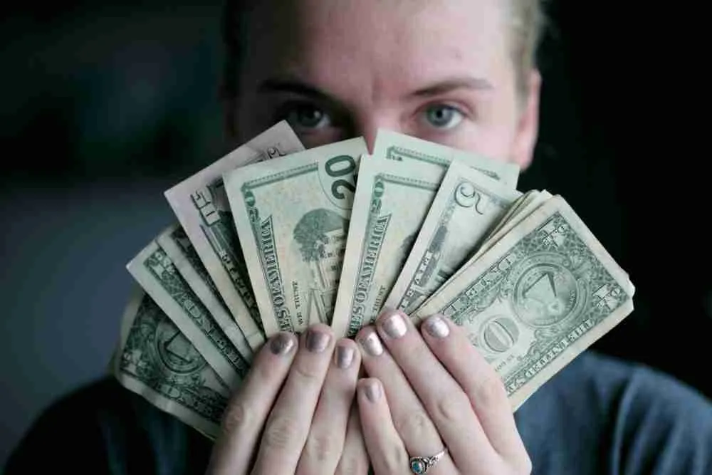 A person with a playful expression fanning out an assortment of wage day advance bills in front of their face, with the eyes peering over the money.