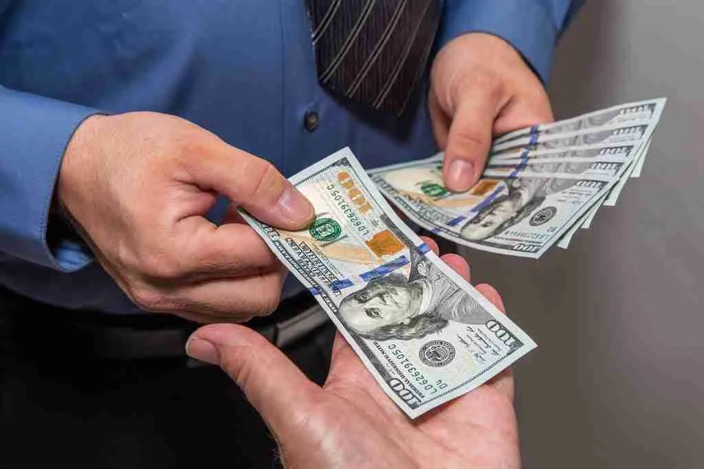 A person in need of an $11000 loan counts US dollar bills carefully in a blue shirt.