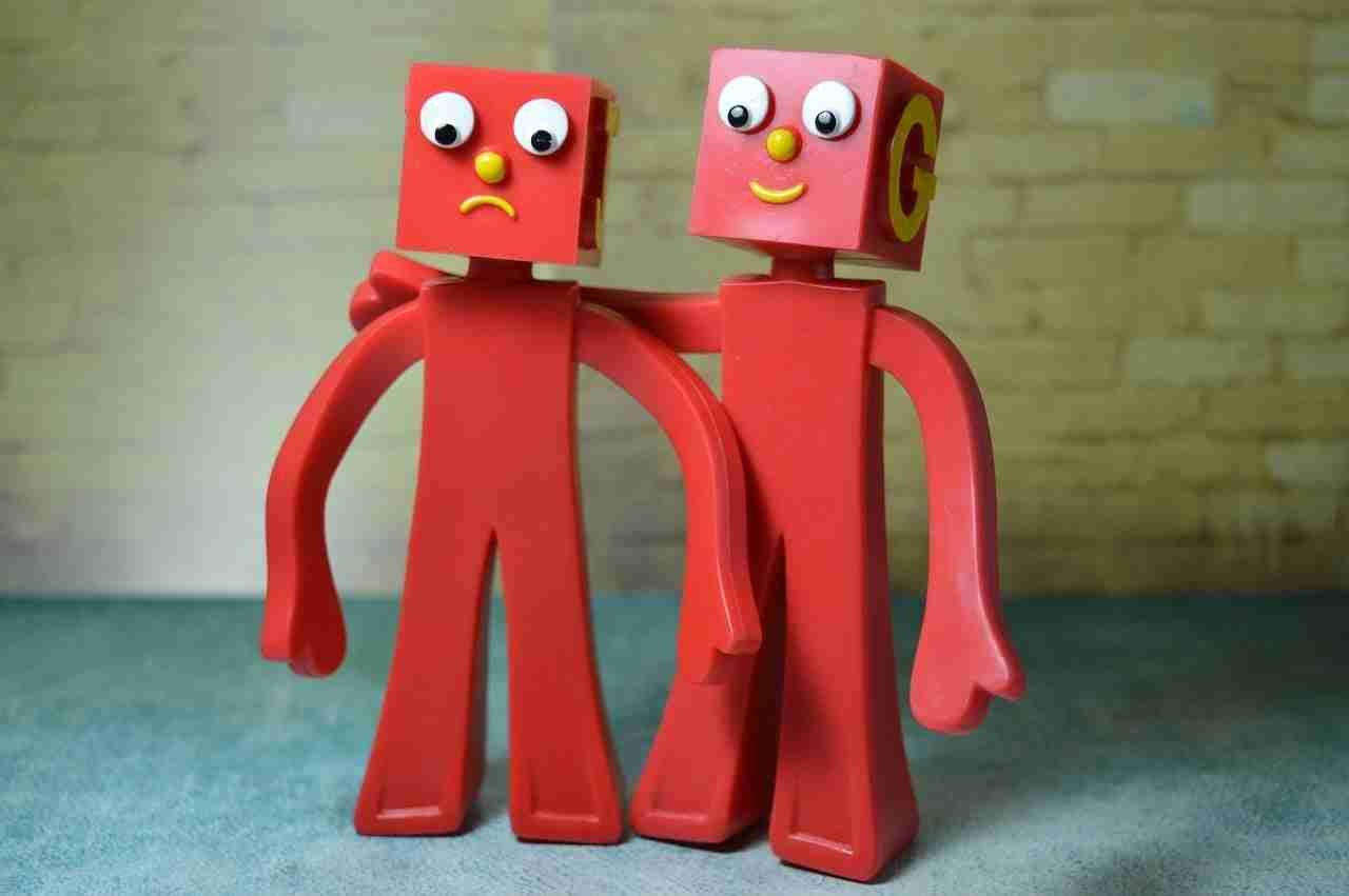Two whimsical red plastic figures with googly eyes and alphabet letters on their heads standing side by side against a pastel background. buddy loans.