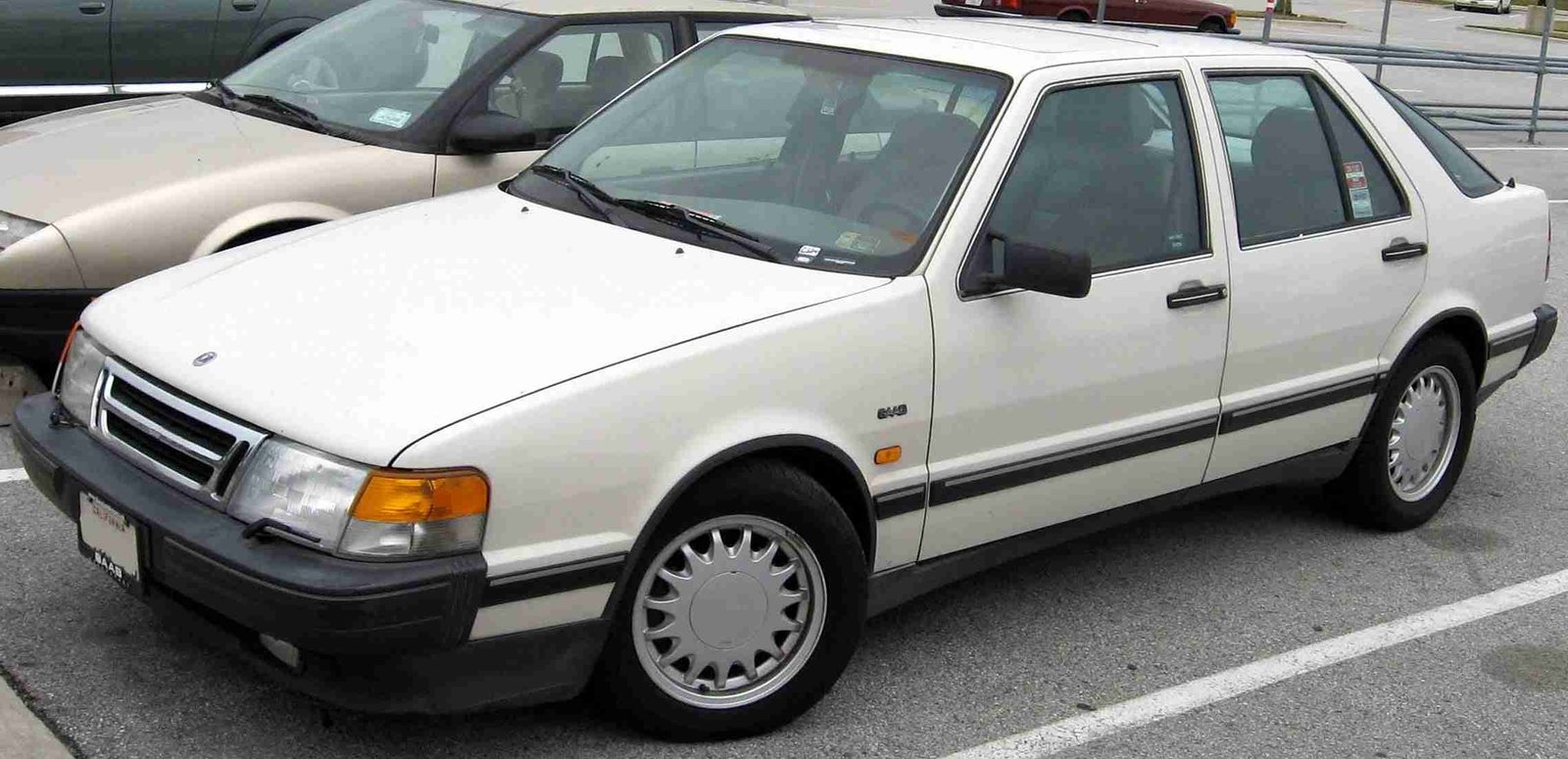 A white four-door sedan parked in a parking lot with other cars in the background.